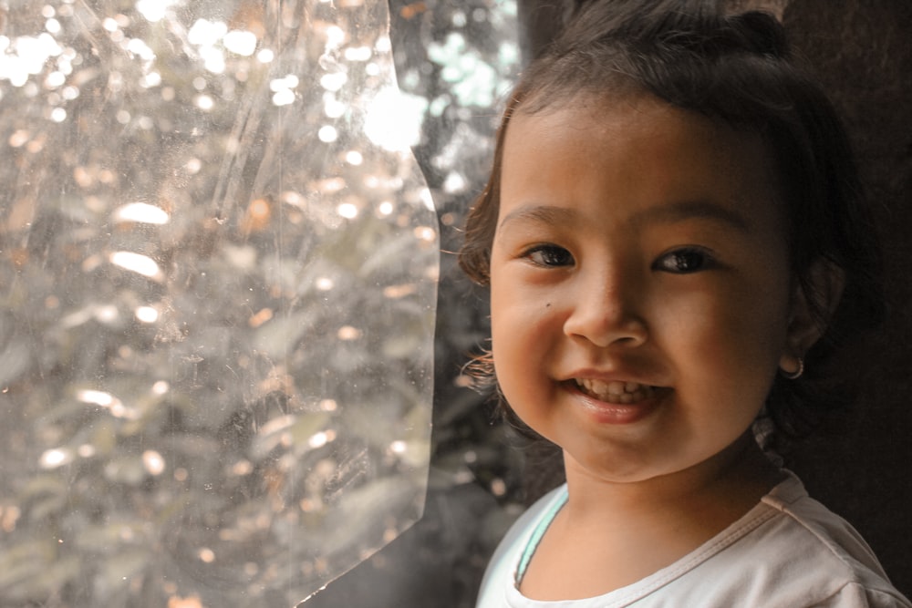 Una niña sonriendo con un árbol en el fondo