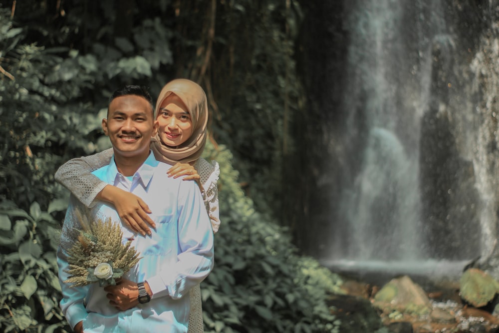 a man and woman hugging in front of a waterfall