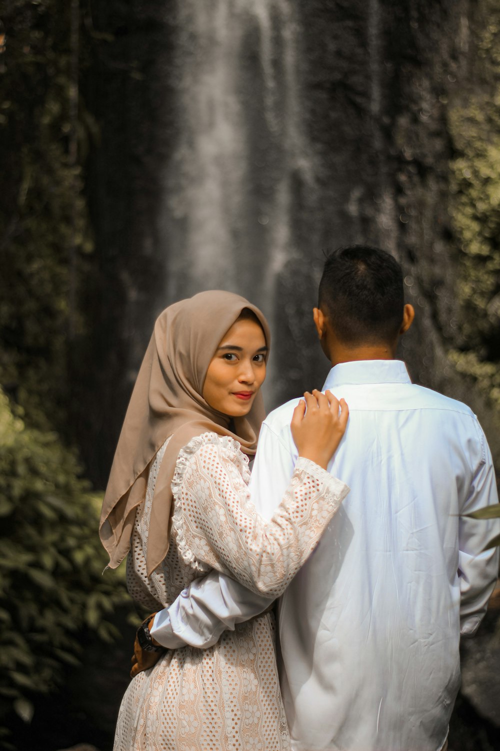 a man and woman standing in front of a waterfall