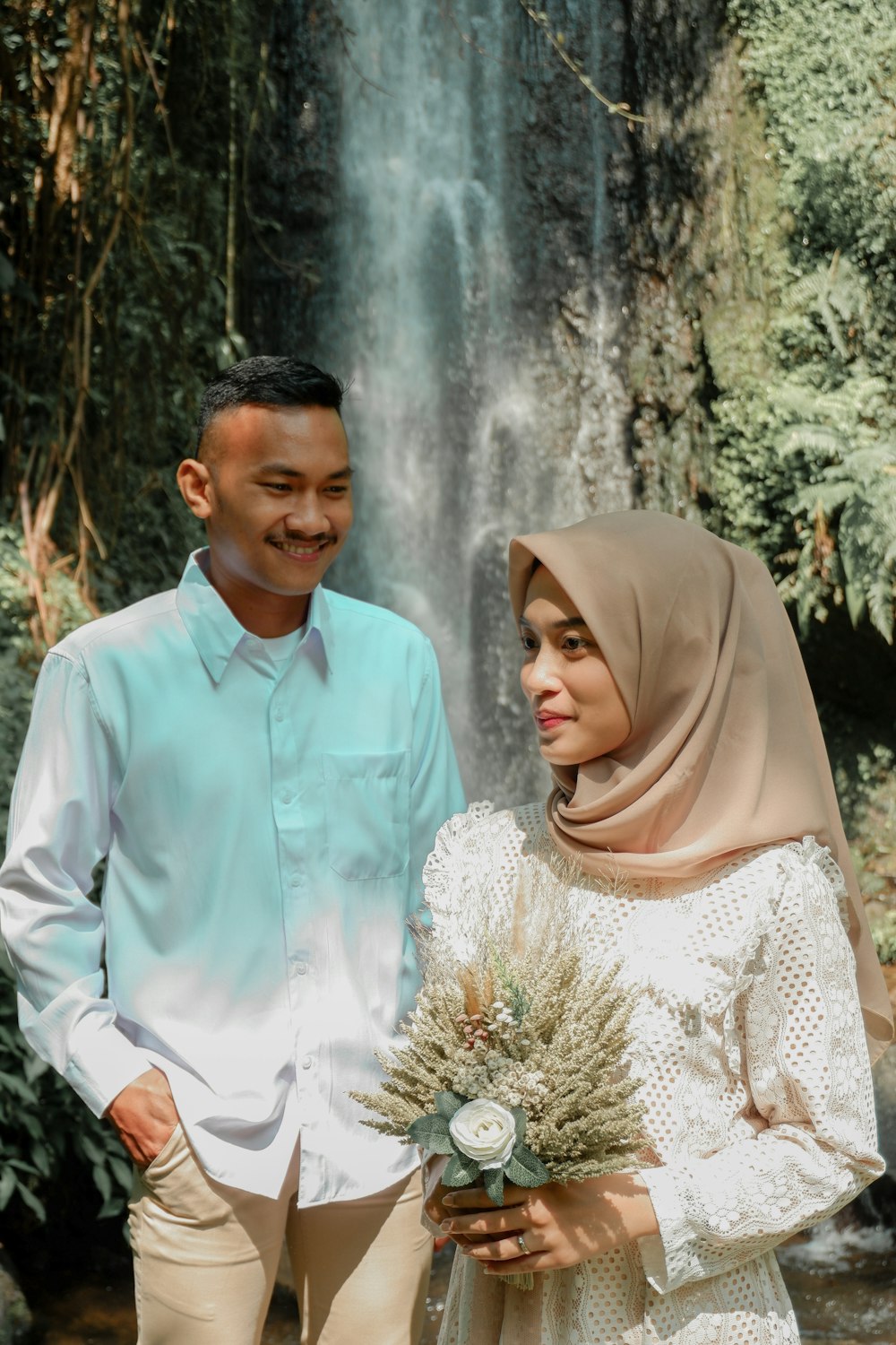 a man and woman posing for a picture in front of a waterfall