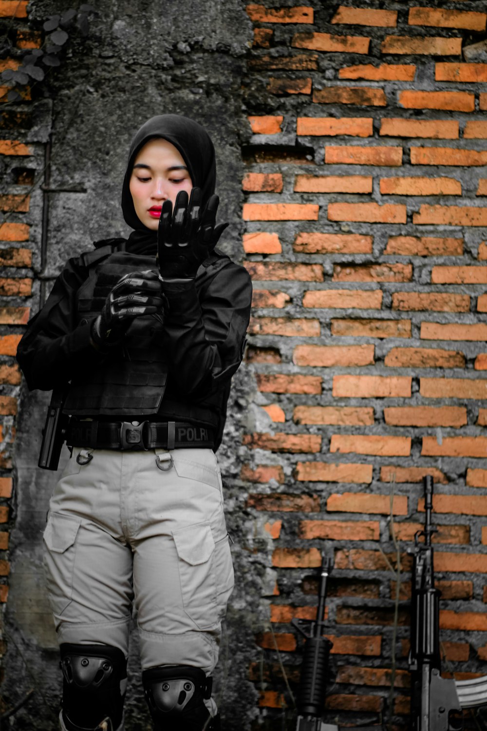 a person in a black jacket and gloves standing in front of a brick wall