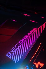 Striking neon lights create a futuristic and vibrant aesthetic, with diagonal stripes and the text 'NEO DREAMS'. The image uses contrasting colors like pink, red, and blue on a dark background.