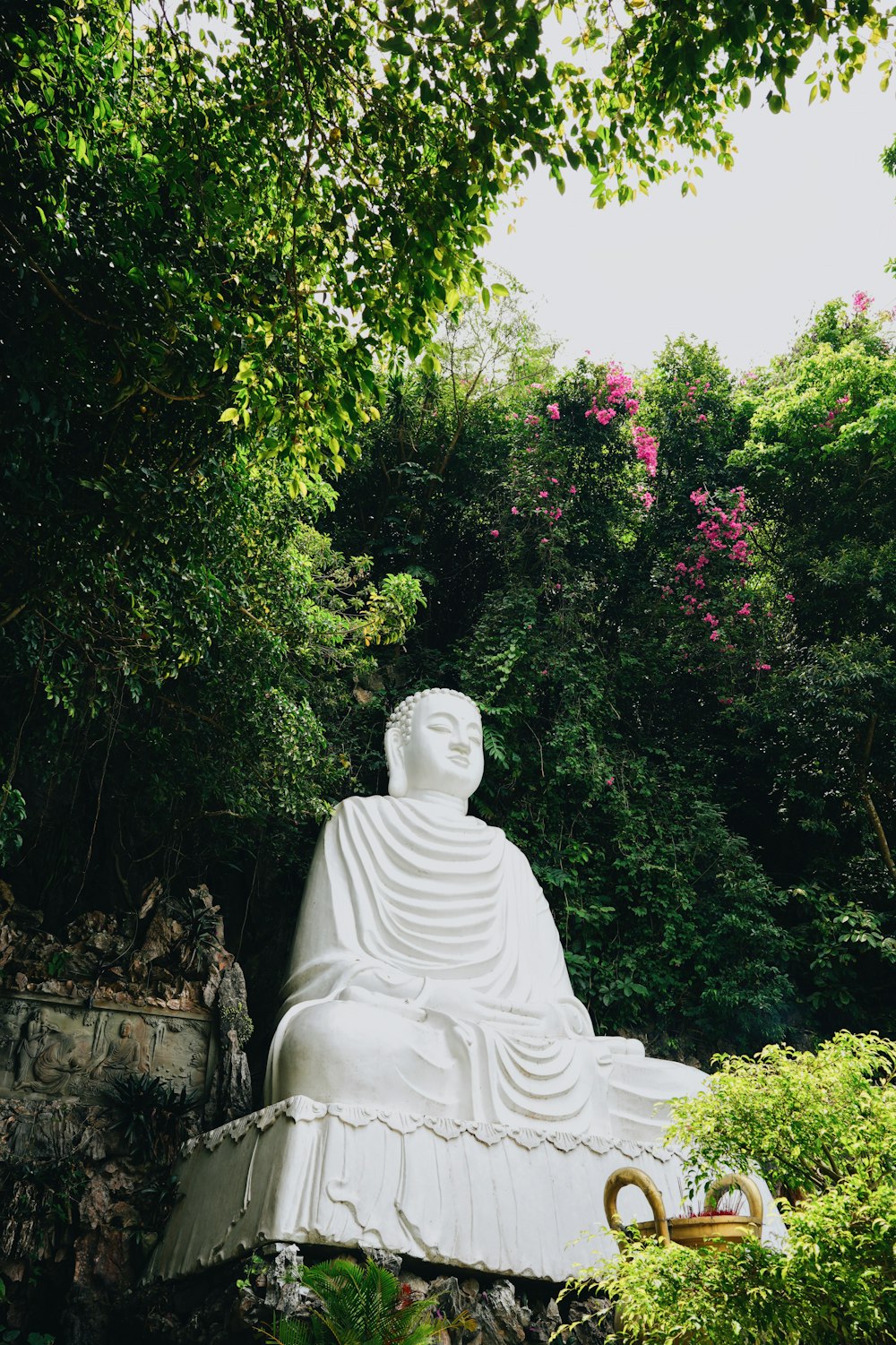 una statua di una persona seduta su una panchina in un giardino