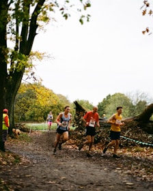 a group of people running on a dirt path with trees and grass