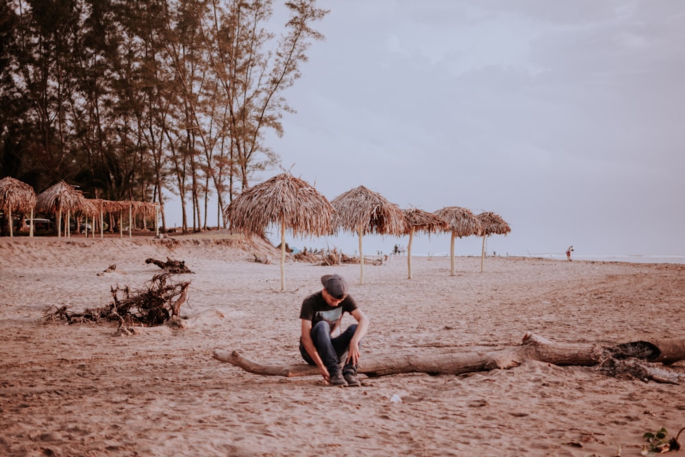 a man and woman sitting on a beach with straw umbrellas