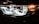 Close-up view of a car's headlight, featuring intricate LED design and reflective surfaces. The light emits a bright, white glow, accented by amber lighting on the side.