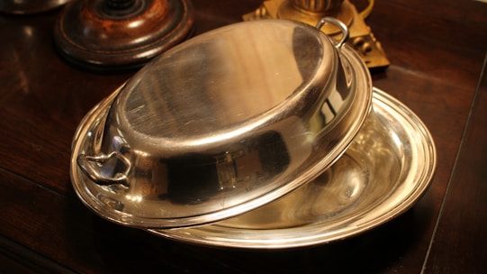 Close-up of a polished brass chafing dish with intricate artisan details on a cream linen tablecloth.