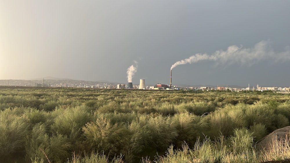 a field with smoke stacks and a factory in the background