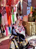A vintage photo of young Samia Shabo at her first small business stall, surrounded by colorful goods.