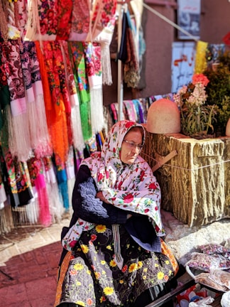 A vintage photo of young Samia Shabo at her first small business stall, surrounded by colorful goods.