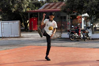 A content creator holding a camera, capturing a football freestyle sequence in an urban setting.