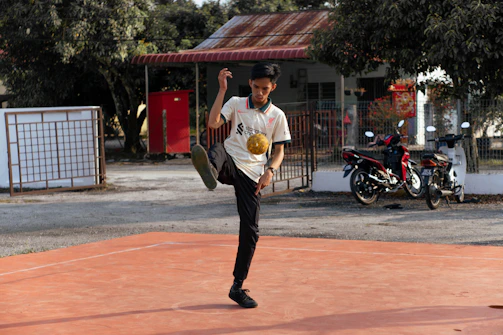 An influencer filming football tricks with a smartphone against an urban backdrop.