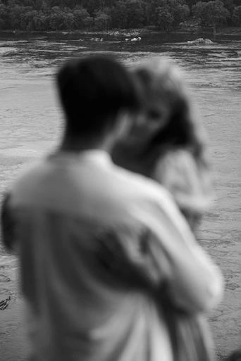 a man and woman kissing in front of a lake