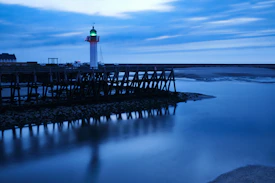 A serene navy blue lighthouse shining golden beams over a calm sea at dawn.