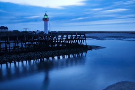 A serene navy blue lighthouse shining golden beams over a calm sea at dawn.