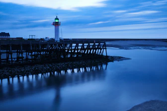 A serene navy blue lighthouse shining golden beams over a calm sea at dawn.
