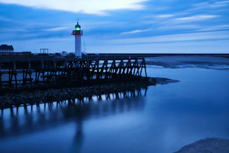 A serene navy blue lighthouse shining golden beams over calm ocean waters at dusk.