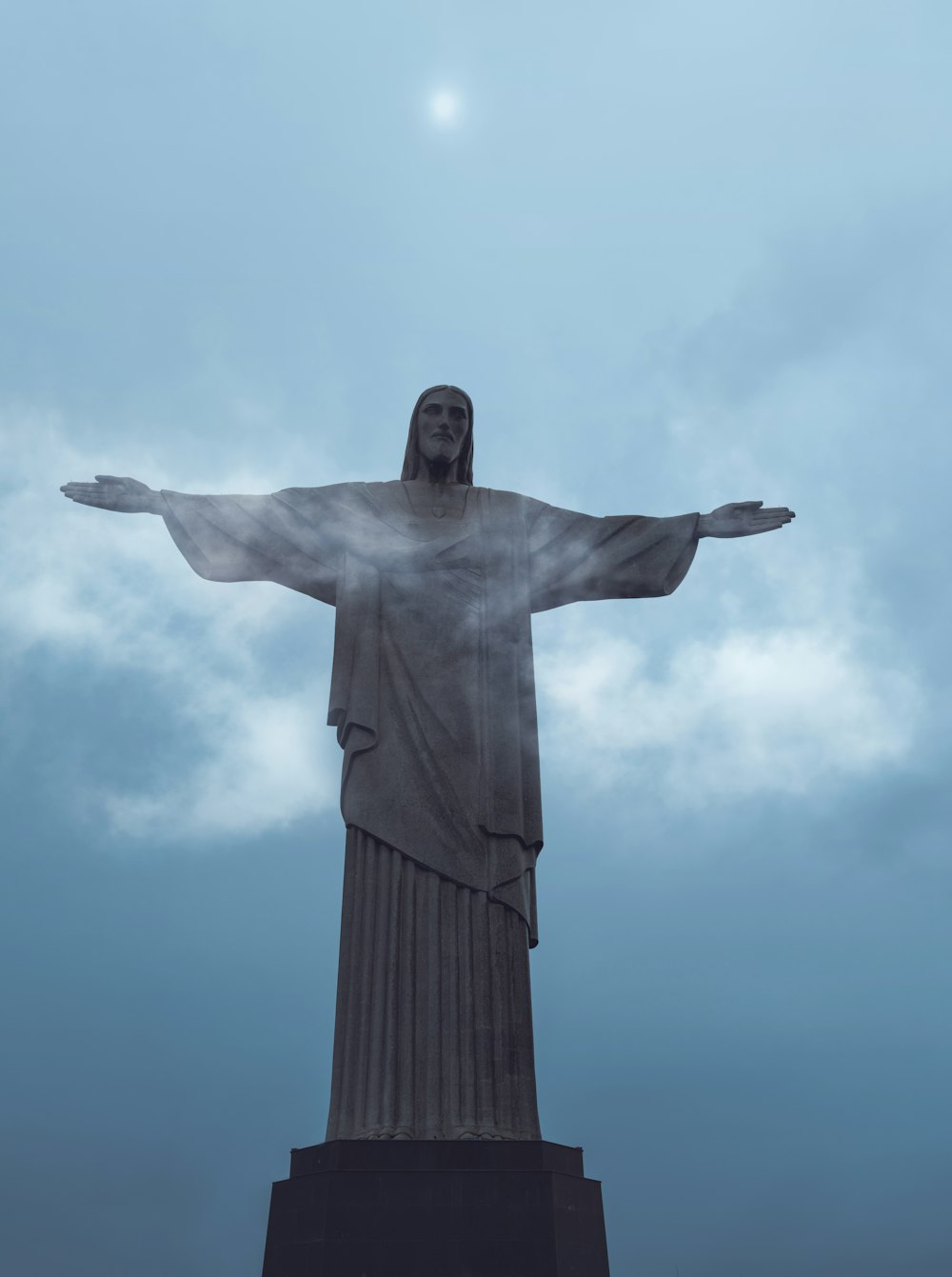 uma estátua de uma pessoa segurando os braços com o Cristo Redentor ao fundo