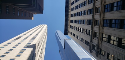 Several tall skyscrapers converge towards a bright blue sky in a cityscape with buildings of varying architectural styles.
