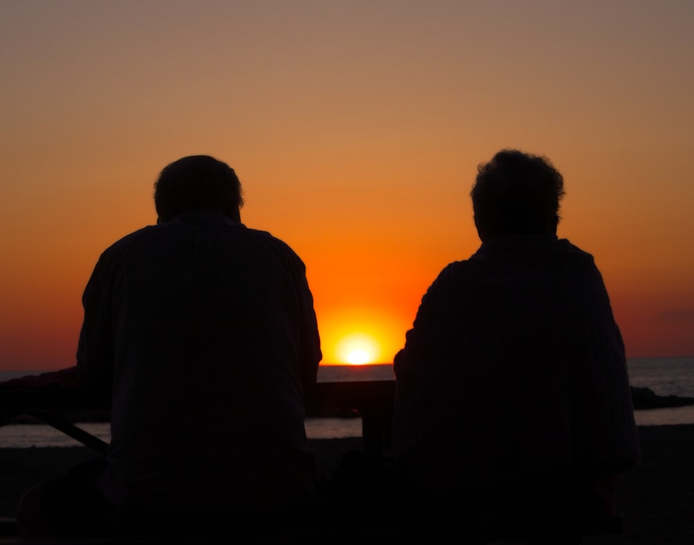a couple of people sitting in front of a sunset