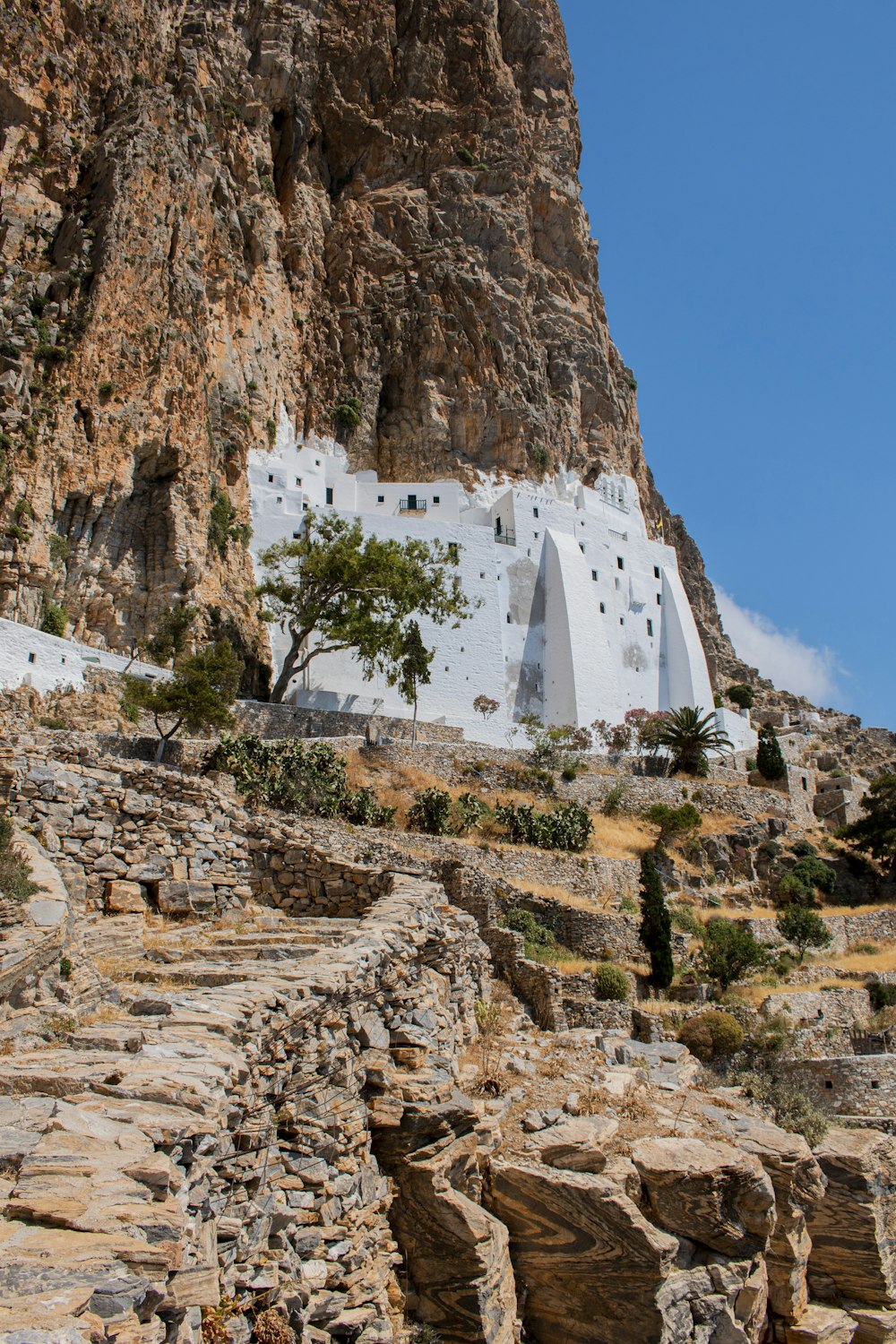 a stone building on a cliff with Amorgos in the background