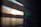 Horizontal slats of window blinds partially open, allowing light to filter through, creating a soft, diffused glow with shadows and highlights.