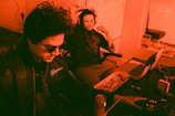 Robod5 and guest artist vibing in a studio surrounded by synthesizers and mixing gear.