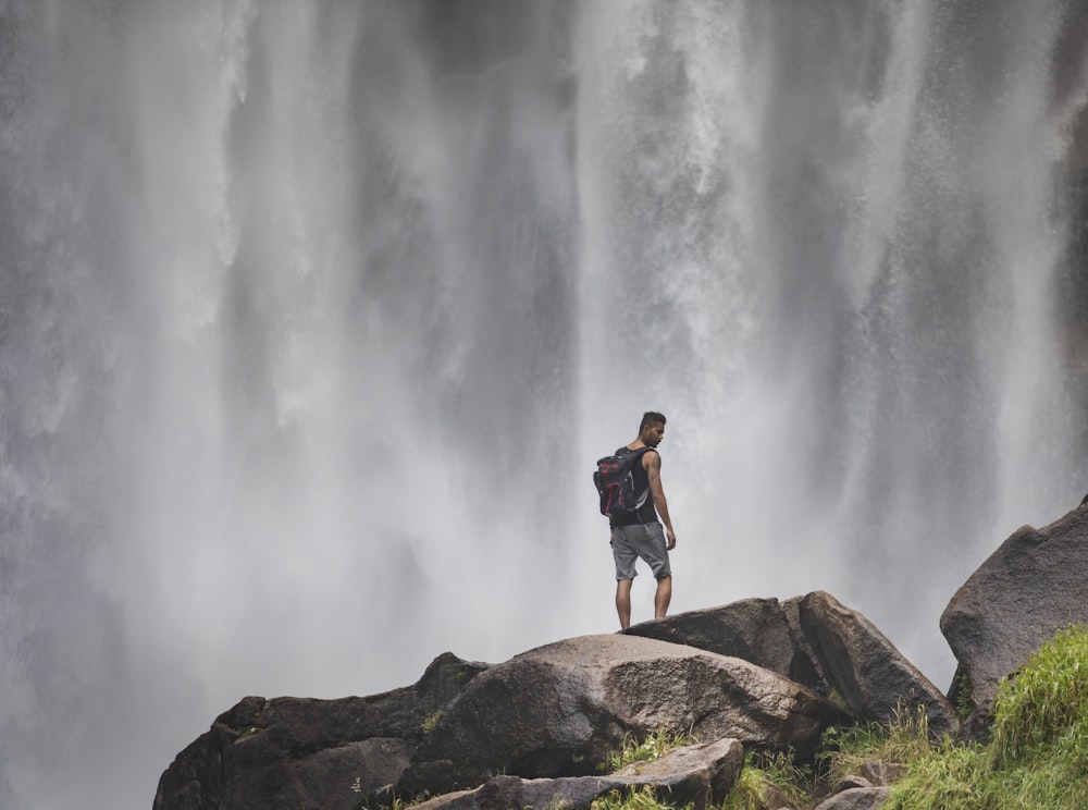 a man standing on a rock in front of a waterfall