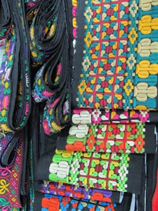 Colorful woven fabric strips with intricate geometric patterns and various colors such as red, green, blue, orange, and yellow against a dark background.