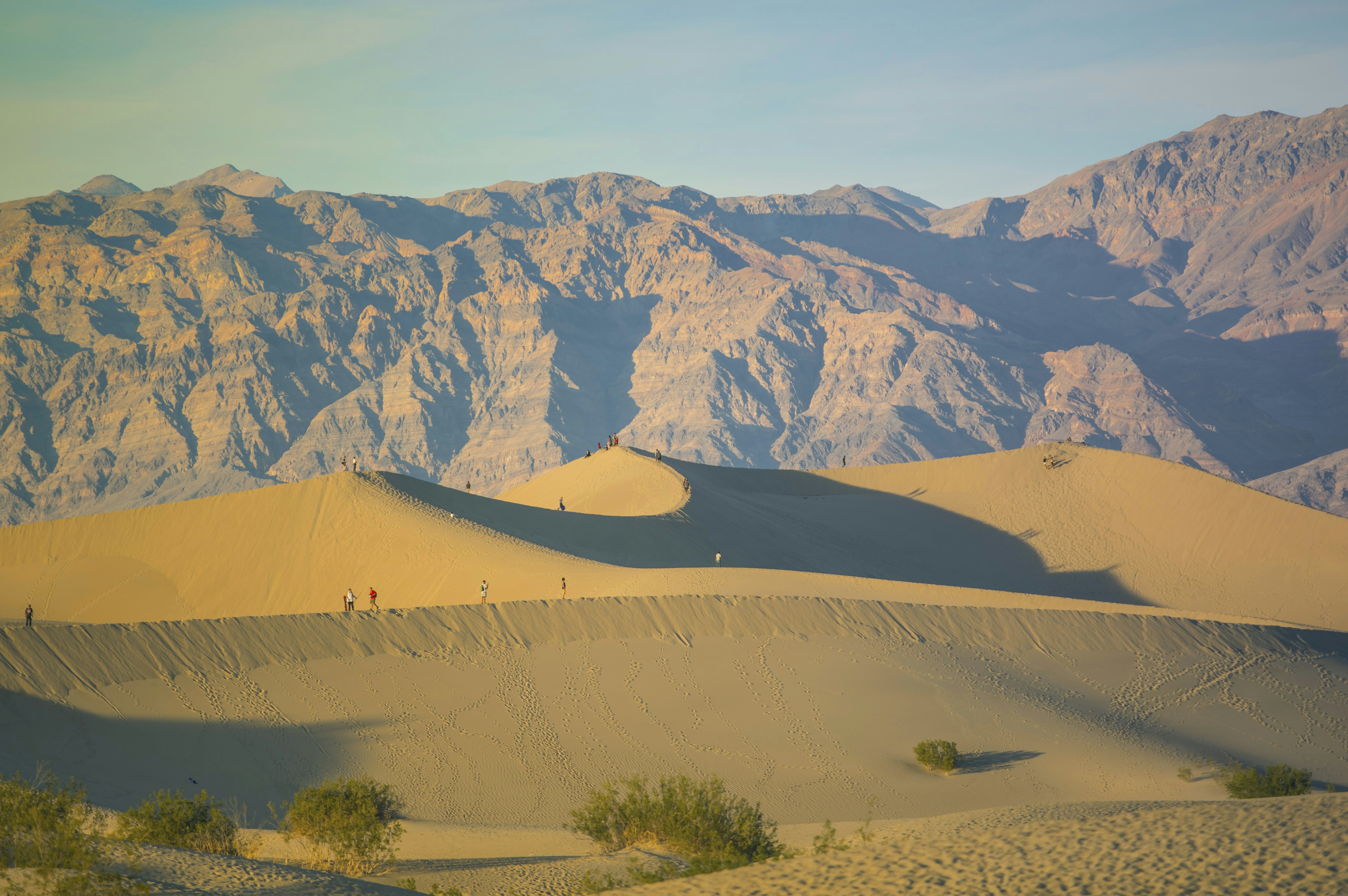 a group of people walking on a sand dune in front of a large mountain