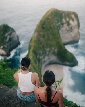 two women sitting on a rock overlooking a body of water
