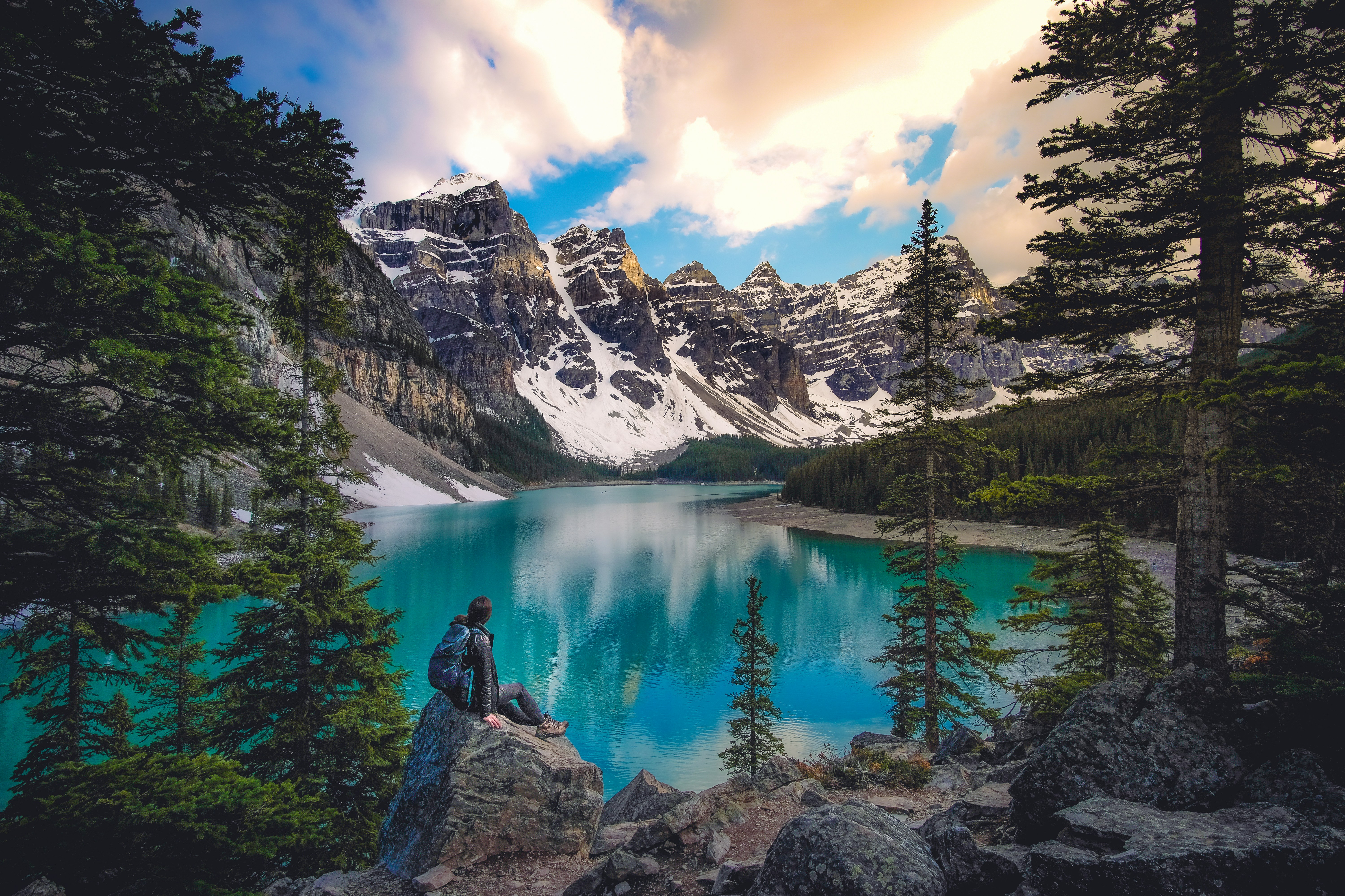 a person sitting on a rock by a lake surrounded by mountains