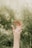 Two hands are reaching upward, surrounded by a natural, blurred green background. The focus is on the hands, which appear gentle and graceful, suggesting themes of connection or reaching out.