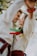 A couple dressed in traditional clothing shares an intimate moment, with ribbons in various colors attached to their garments. The background is blurred, highlighting the focus on the couple and creating a warm, joyful atmosphere.