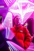 Model wearing a sleek black jacket with red accents standing under neon lights at night.