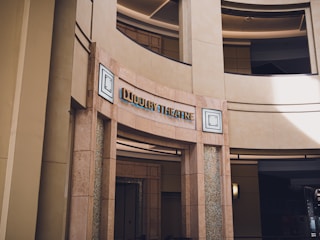 An entrance to a building labeled 'Dolby Theatre' with architectural features including rounded walls and columns. The signage has modern lettering, and there are decorative mosaic patterns flanking the entrance.