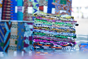 Stacks of colorful apparel and vibrant fabrics piled in a textile market stall.