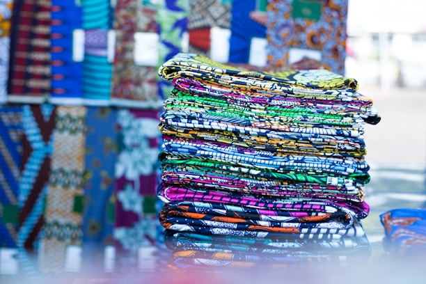 Close-up of colorful, textured African fabric rolls stacked neatly in a market setting.