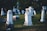 A serene graveyard with several white tombstones set against a backdrop of green grass and trees. The stones vary in height and design, with some having crosses on top. Soft sunlight casts gentle shadows, creating a peaceful and solemn atmosphere.