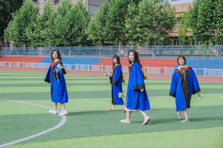 a group of girls in blue gowns on a grass field