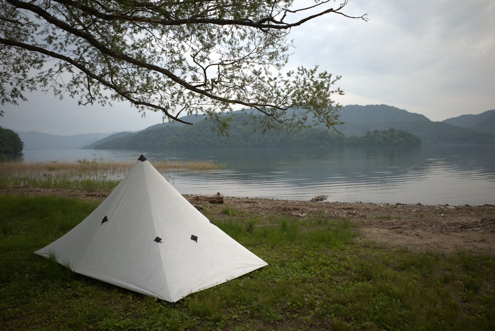 a white tent on a grassy hill by a body of water