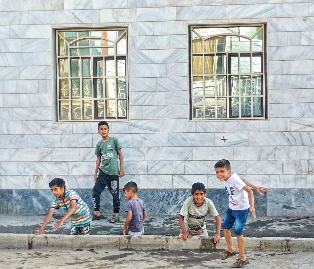 a group of boys sitting on a curb in front of a building