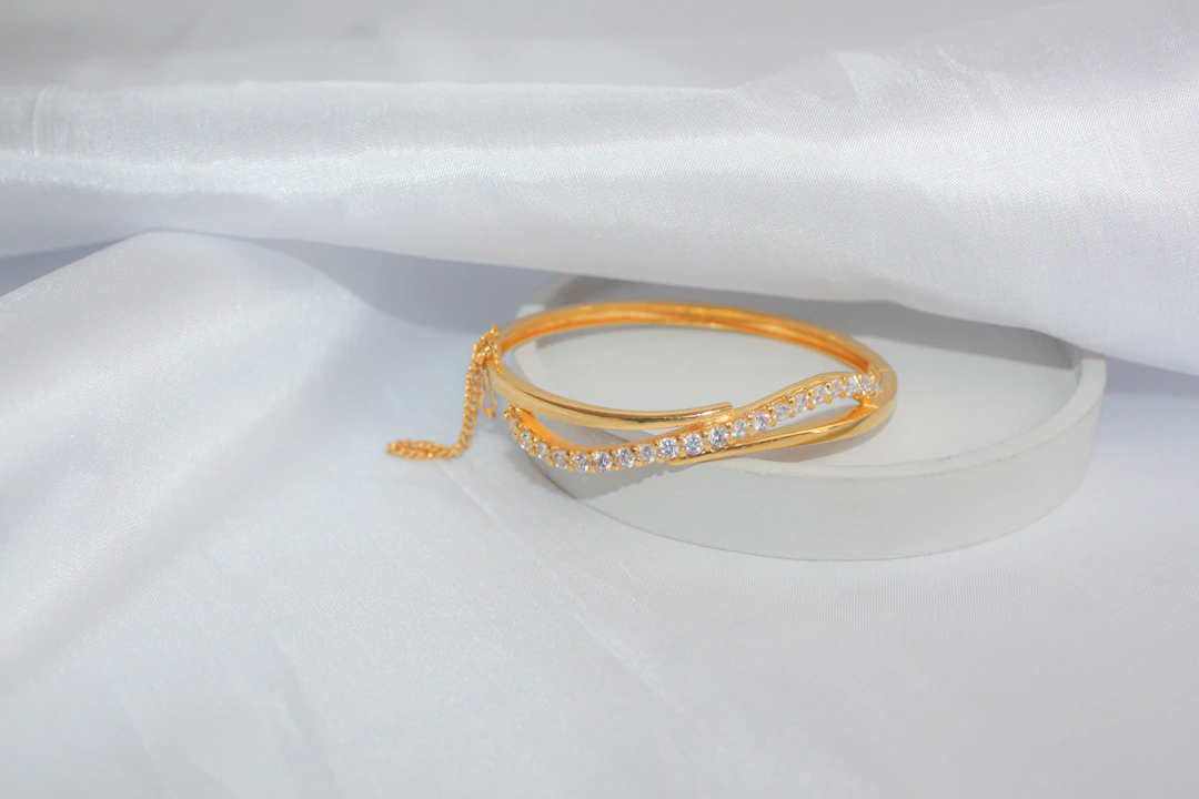 Bracelete dourado com zircônias sobre tecido branco.