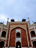 An architectural view of a historical monument featuring intricate geometric patterns and designs. The structure is composed of red sandstone with white marble accents and arches, showcasing traditional craftsmanship. The sky forms a muted backdrop, enhancing the monument's grandeur.