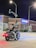 A motorcyclist wearing a black vest with colorful patches is stopped at a nighttime intersection in front of a Chase bank. The scene is illuminated by streetlights and traffic signals, and the motorbike has red lights turned on. The bank building is made of brick and has large windows, with a blue neon sign displaying the word 'CHASE'. There are some plants in front of the bank, and the street signs indicate the intersection of Centralia and 59th Ave.