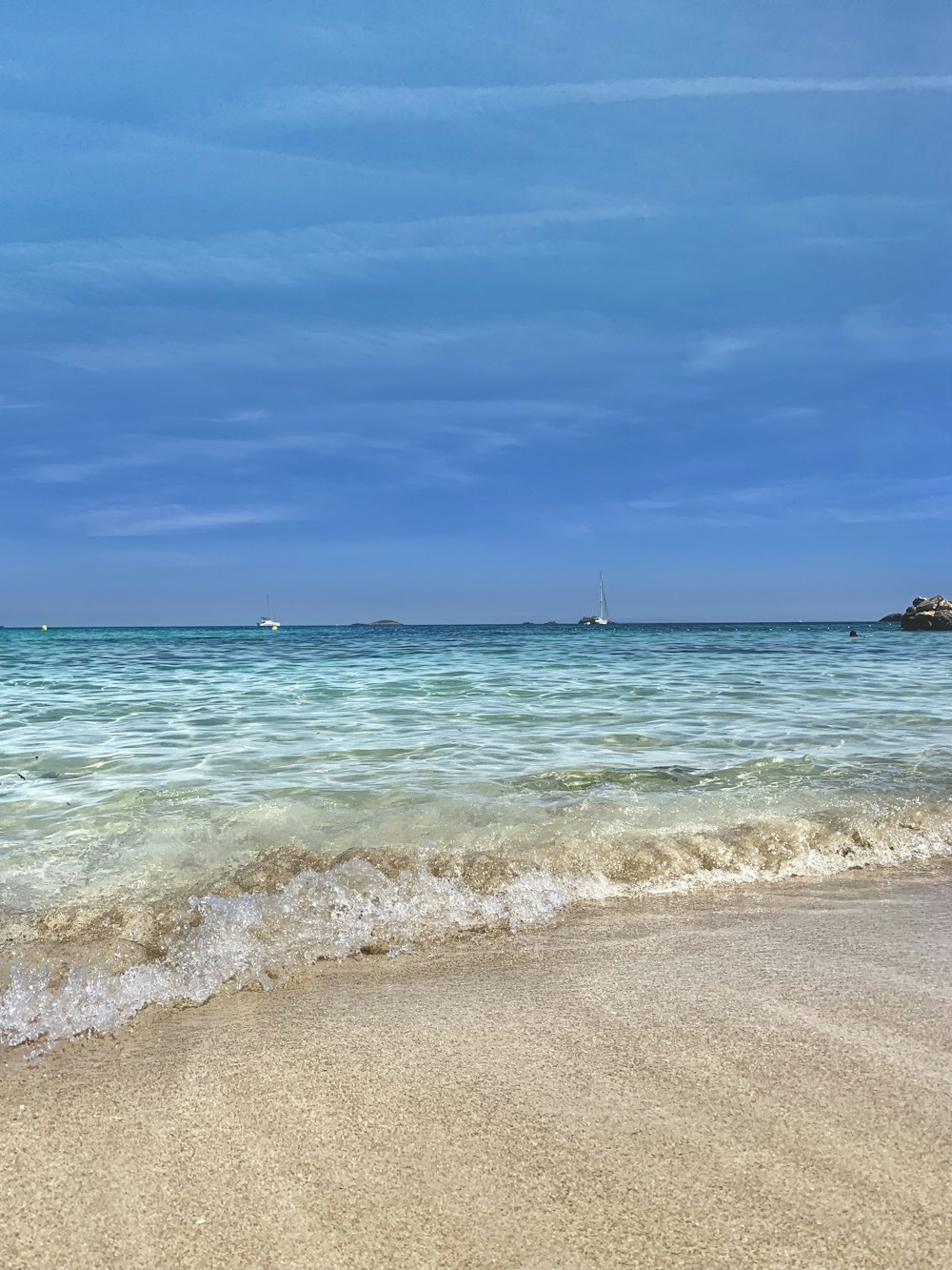 a beach with waves and a sailboat in the distance