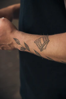 Black line art tattoo depicting the outlines of the 25 de Abril bridge on a forearm