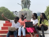 a group of people sitting on a bench with laptops