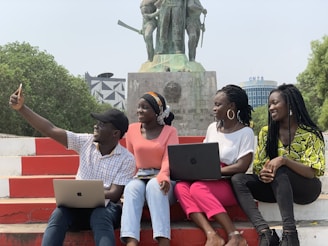 a group of people sitting on a bench with laptops