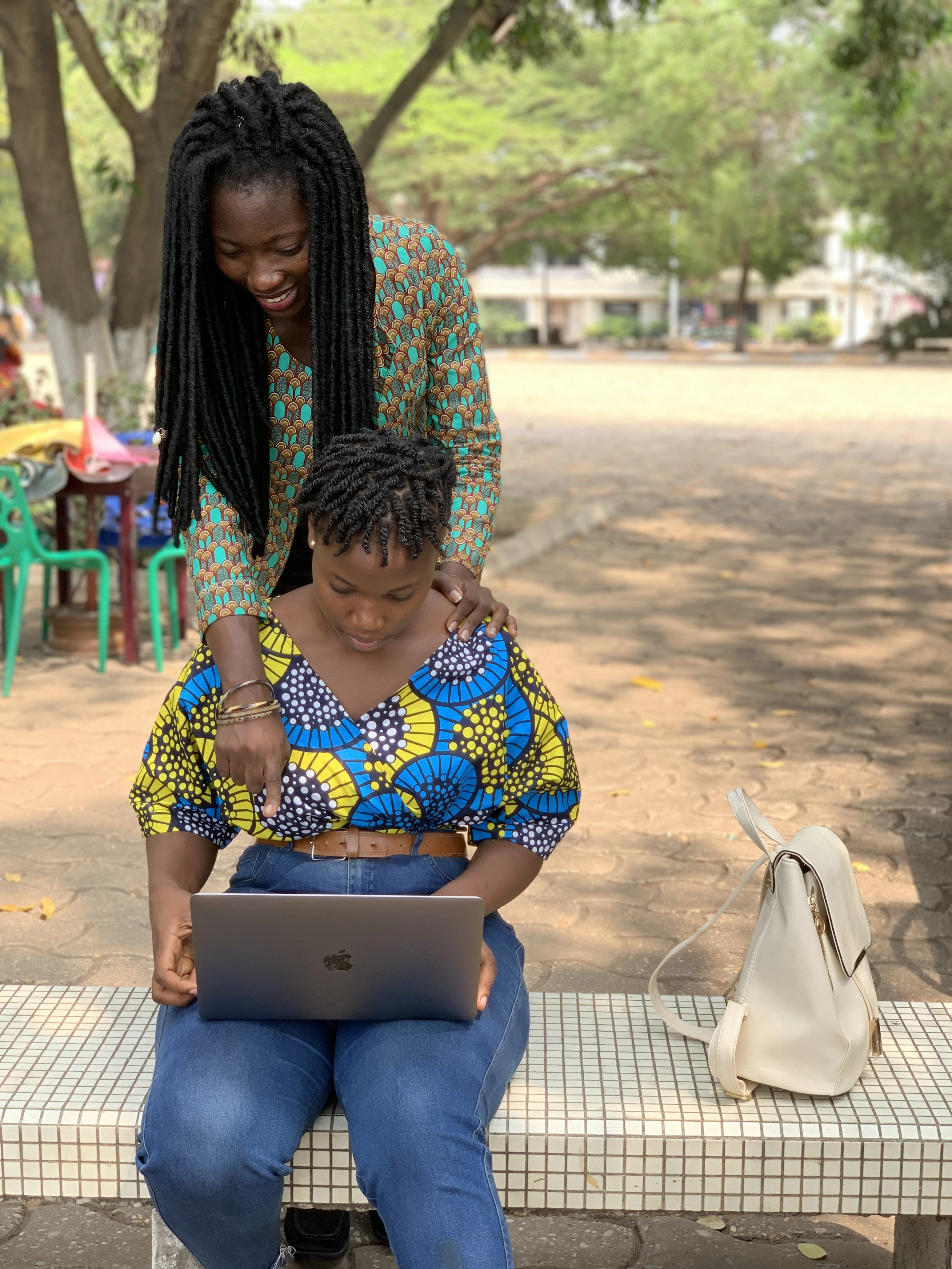A woman sitting outdoors with a laptop open on her lap, a bag beside her